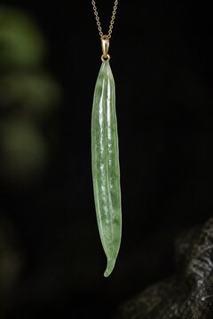 A slender green jade pendant shaped like a silique on a dark background.