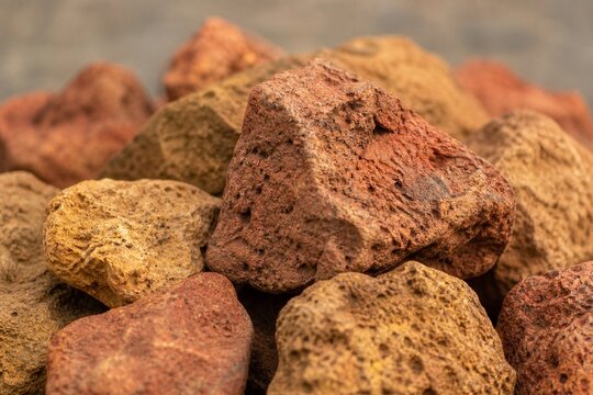 Pile of rough ochre bauxite ore samples in red and yellow, close-up with shallow focus.