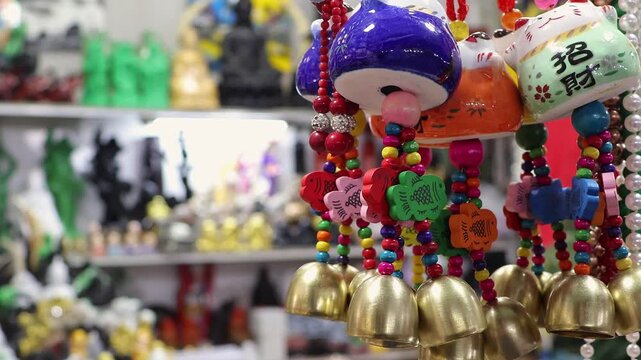 Traditional Vietnamese wind chimes with brass bells and lucky cat amulets hanging at Nha Trang night market, Vietnam. Colorful ceramic souvenirs displayed at local gift street shop. Tourism concept.