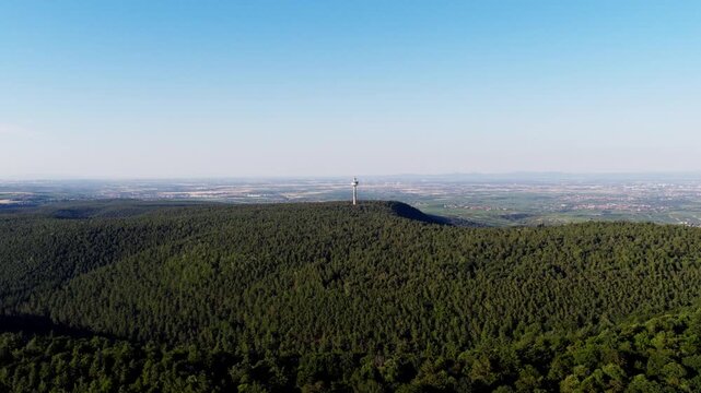 Aerial View of a Forested Hill with Communication Tower Against a Blue Sky and Distant Horizon