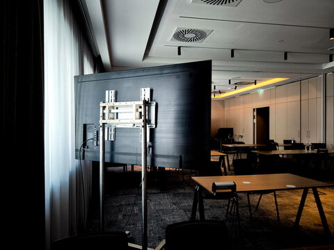 Back view of large flat screen monitor with wall mount bracket in modern Munich conference room, presentation technology setup near window and curtains, business meeting equipment and AV installation 