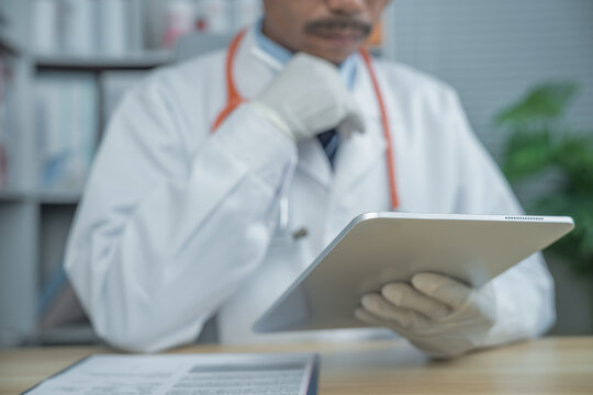 Middle Eastern male doctor with mustache reviewing patient records on a digital tablet in a modern clinic. Professional healthcare consultation, electronic medical records and telemedicine concept.