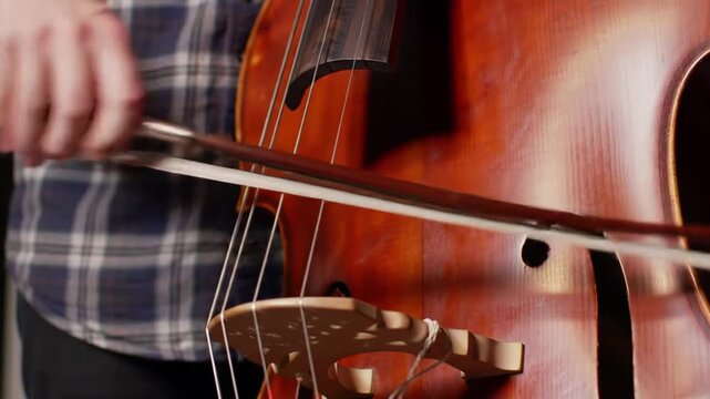 Close-up of a person playing the cello with a bow, classical music instrument.