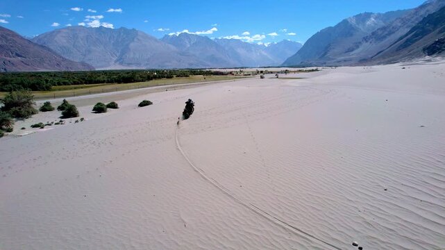 Motorcyclist Traverses Sandy Valley. Motorcycle Crosses Expansive Sandy Terrain With Distant Hills