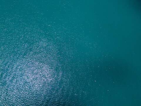 Aerial top down view of turquoise sea water surface with sun glares