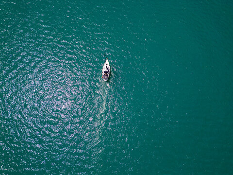 Top down aerial view of sailboat cruising in deep turquoise ocean water