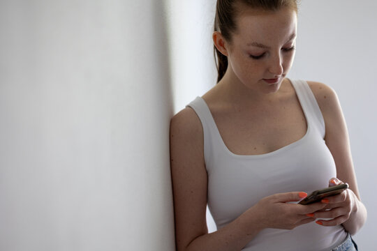 Young Woman Leaning Against Wall While Looking at Smartphone, Concept of Digital Stress and Social Media Anxiety