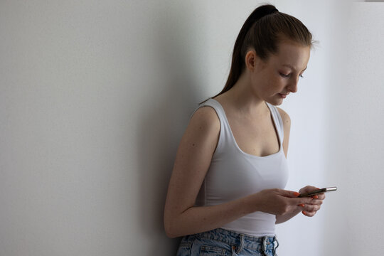 Young Woman Leaning Against Wall While Looking at Smartphone, Concept of Digital Stress and Social Media Anxiety