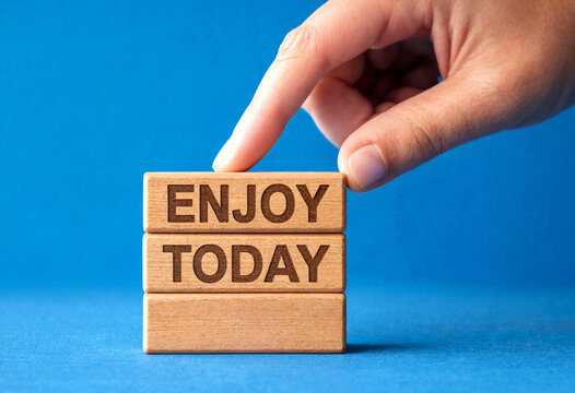 Hand placing the last wooden block with enjoy today text for motivation and positivity concept