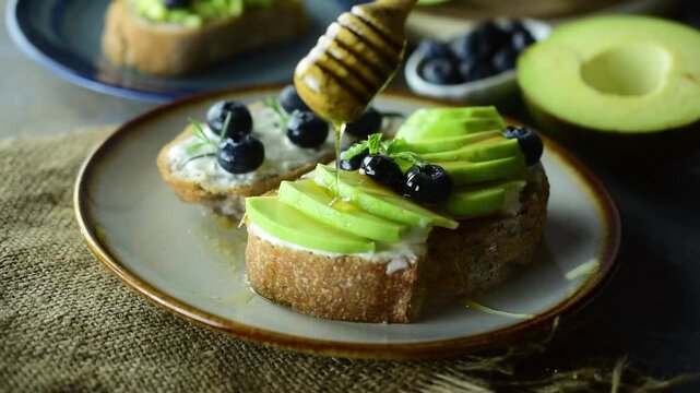 Healthy avocado toast on rustic sourdough bread topped with fresh blueberries, mint leaves, and a drizzle of honey. Perfect for organic breakfast, clean eating, and nutritious gourmet cafe concept