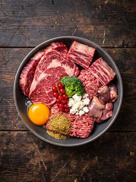 Raw meat assortment with egg yolk and vegetables on a dark wooden surface