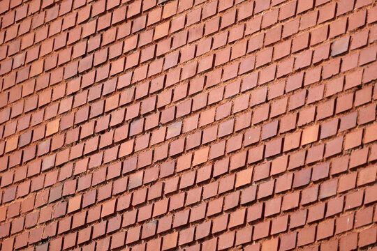 Sunlit red brick wall photographed at an angle, full-frame masonry texture with repeating staggered pattern, rough mortar joints and subtle imperfections, architectural background