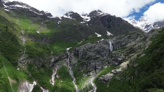 Aerial drone footage approaching Mount Ushba from a distance, revealing Shdugra waterfall in its rocky gorge, Georgia. Snow-capped summit, melting glacier, river below. Original, 4K footage.