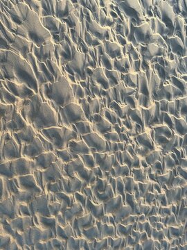 Natural rippled sand texture on a beach with warm sunlight and soft shadows. Abstract background with detailed sandy pattern.