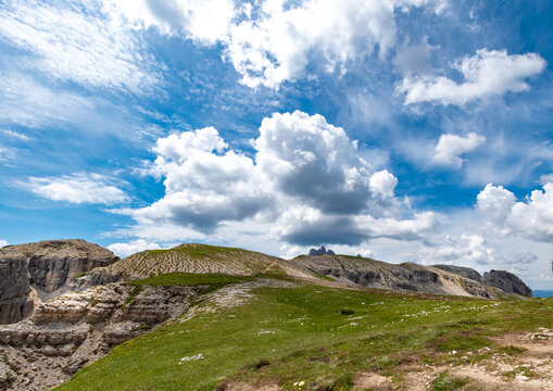 Rolling alpine pastures and rocky mountain ridges under a dramatic sky with fluffy cumulus clouds in the Dolomites, Italy