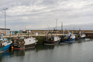 Fototapeta premium Fishing boats moored at Burghead Harbor in Moray, Scotland, under an overcast sky