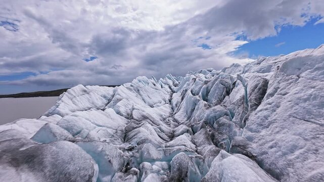 Dynamic FPV drone flight skimming above and between deep glacier crevasses on glacier, Iceland. Cinematic aerial footage revealing blue ice formations and dramatic glacial landscape.