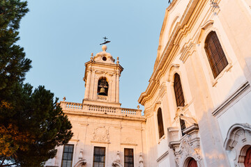 Fototapeta premium Sunlit baroque church facade and bell tower in Lisbon, framed by pine branches against a clear blue sky.