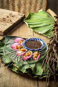 Delicious Miang Kham Bua Luan, a traditional Royal Thai appetizer featuring vibrant pink lotus petals, toasted coconut, fresh herbs, and sweet savory dipping sauce served on a wooden table.