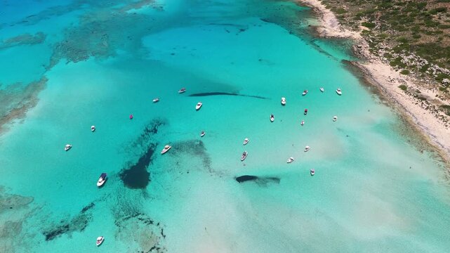 Overhead aerial drone view of boats anchored in the clear turquoise shallows along the sandy shore of Balos Lagoon, Balos, Greece
