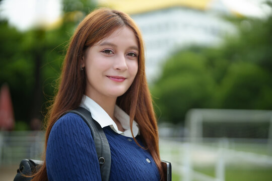 Portrait of a teenage female student smiling at the camera while standing outdoors on a school or university campus.