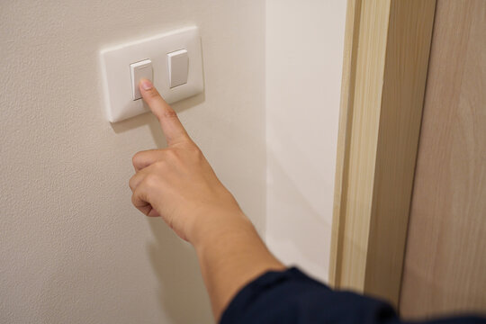 Close up of a hand turning off a light switch at home, representing energy saving, electricity conservation and sustainable living.