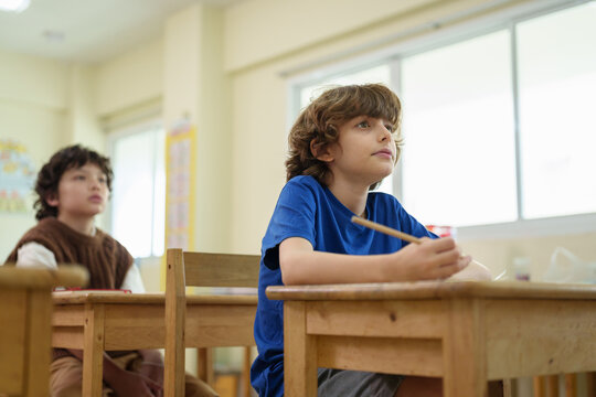 Focused caucasian schoolboy listening carefully during a classroom lesson while studying with classmates in a multicultural school environment.