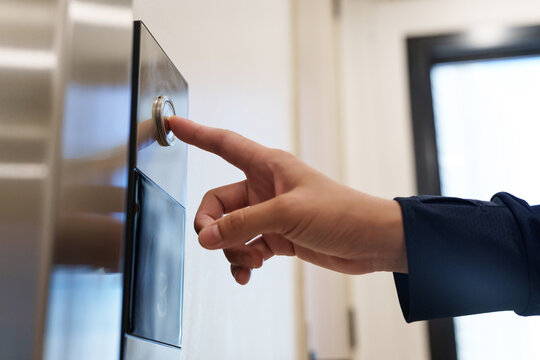 Close up of a hand pressing an elevator button in a modern building, representing transportation and daily commuting.