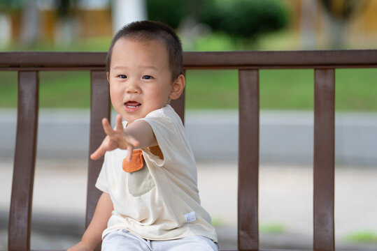 Happy Asian toddler reaching toward camera in park