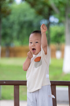 Toddler raising arm against green park background
