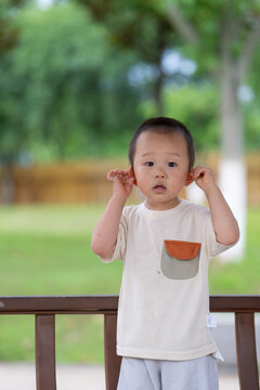 Happy Asian boy holding ears in park