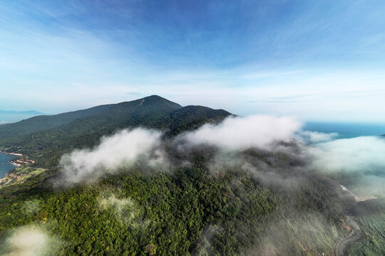 Aerial view shows Son Tra peninsula tropical jungle, with clouds hugging mountains and meeting the ocean coast in Da Nang, Vietnam