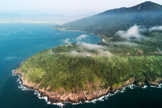 Son Tra peninsula in Da Nang, Vietnam, covered in dense jungle meets the clear ocean waters. Mist hangs over the tropical coast, seen from an aerial perspective