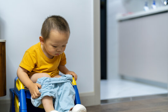 Asian toddler sitting on potty chair at home