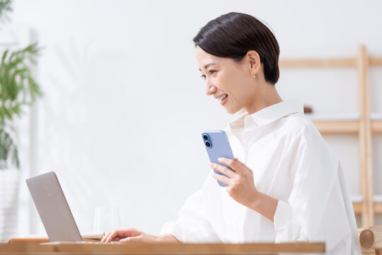 スマホを持ってパソコンを使う女性