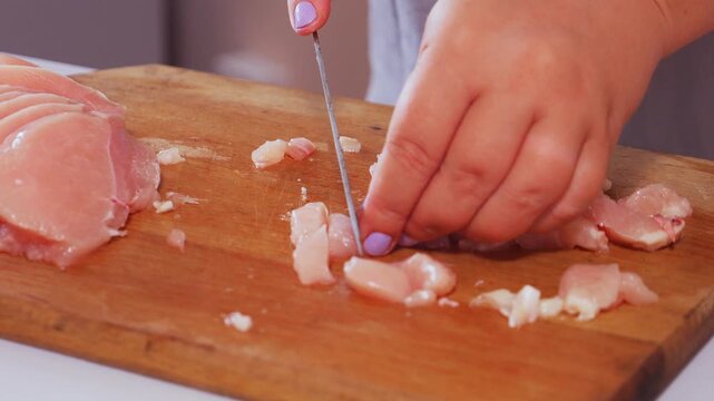 A woman's hands cut a chicken fillet into pieces on a cutting board