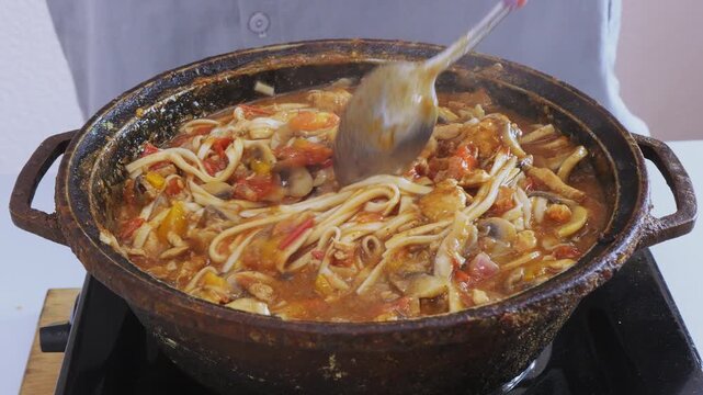 Vegetables with chicken and udon simmer in a cast iron skillet