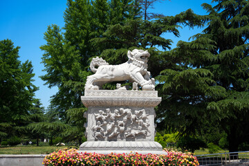 Obraz premium White stone lion sculpture standing amidst flowerbeds and green trees in a park