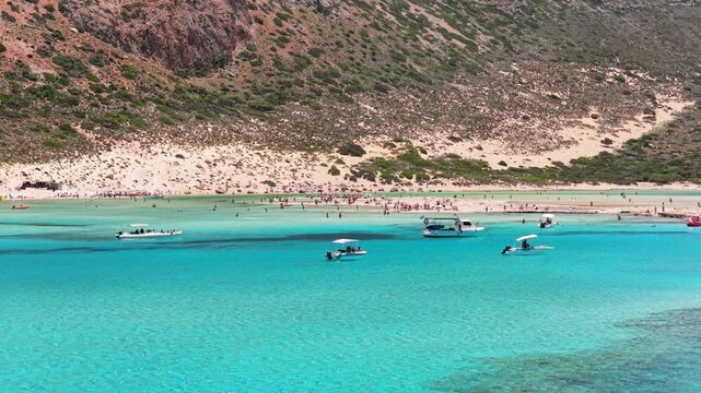Aerial drone view of Balos Lagoon with bathers on the sandy shallows below the steep mountain slope