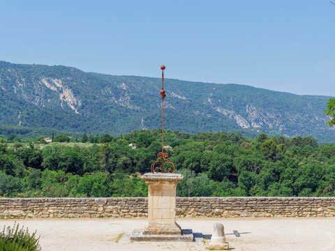 M&eacute;nerbes in Vaucluse. Church square. A wrought iron cross fixed to a square base of white limestone facing the Luberon mountains and verdant state forest