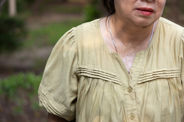 senior asian woman sweating heavily from hot summer weather in a park during daytime, elderly heat...