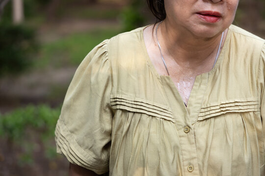 senior asian woman sweating heavily from hot summer weather in a park during daytime, elderly heat exhaustion sweating neck closeup shot