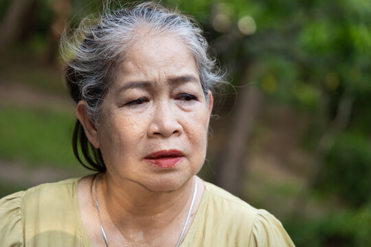 Old asian senior woman looking tired, flushed and sweating from summer heat outdoors, portrait of perspiration and discomfort in natural setting, realistic hot summer lifestyle shot