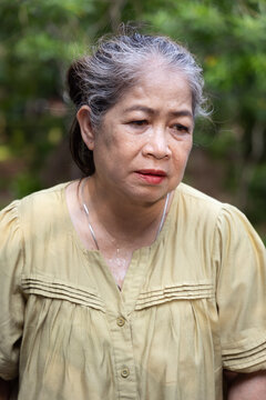 Old asian senior woman looking tired, flushed and sweating from summer heat outdoors, portrait of perspiration and discomfort in natural setting, realistic hot summer lifestyle shot