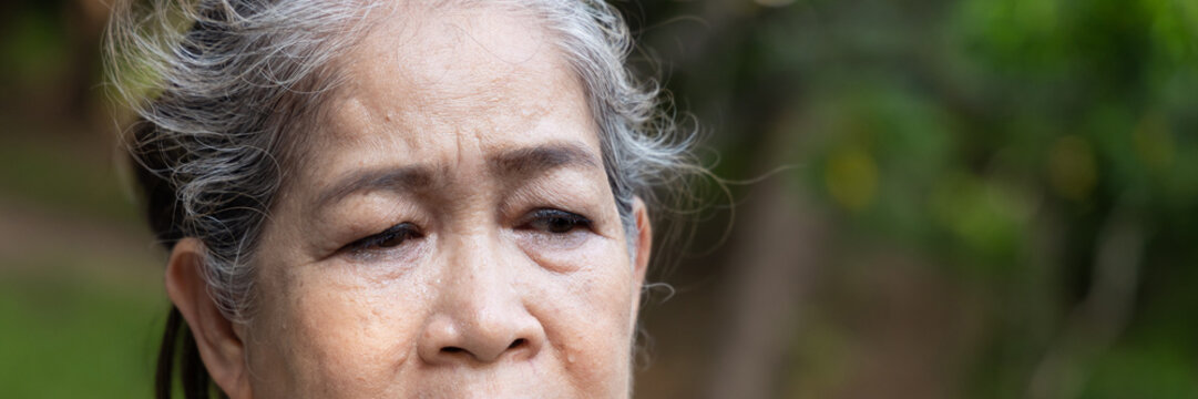 Old asian senior woman looking tired, flushed and sweating from summer heat outdoors, portrait of perspiration and discomfort in natural setting, eye expression closeup shot