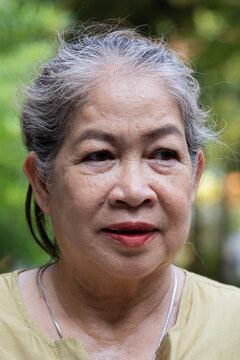 senior asian woman sweating from summer heat in park, taking a deep breath when the wind or breeze is blowing to cope with hot weather, front face closeup view