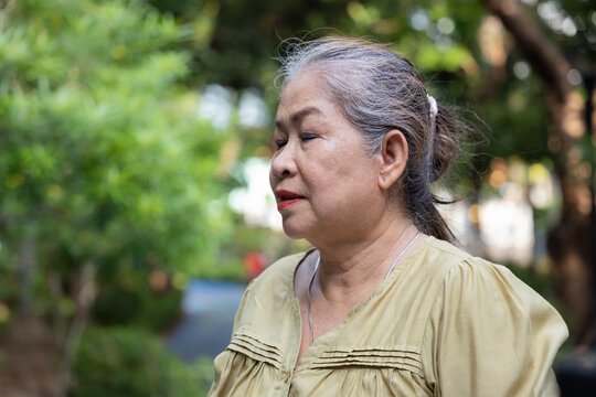 senior asian woman sweating from summer heat in park, taking a deep breath when the wind or breeze is blowing to cope with hot weather, quarter view