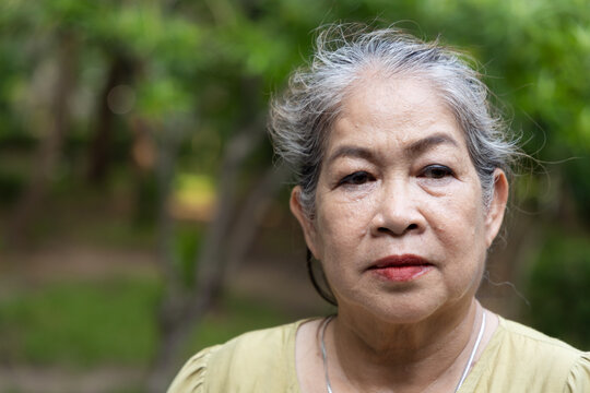 senior asian woman sweating from summer heat in park, taking a deep breath when the wind or breeze is blowing to cope with hot weather, front face closeup view