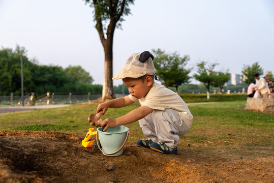 Asian toddler playing with mud and toy bucket in park