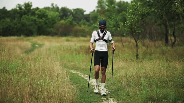 Athlete Walking With Trekking Poles On Grassy Trail. Nordic Walking 